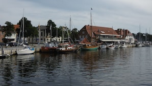 Een jachthaven met verschillende boten afgemeerd, gebouwen met rode daken en een bewolkte lucht.