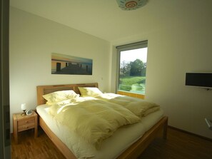Une chambre à coucher avec un lit, une table de chevet, un tableau, une fenêtre et un téléviseur.