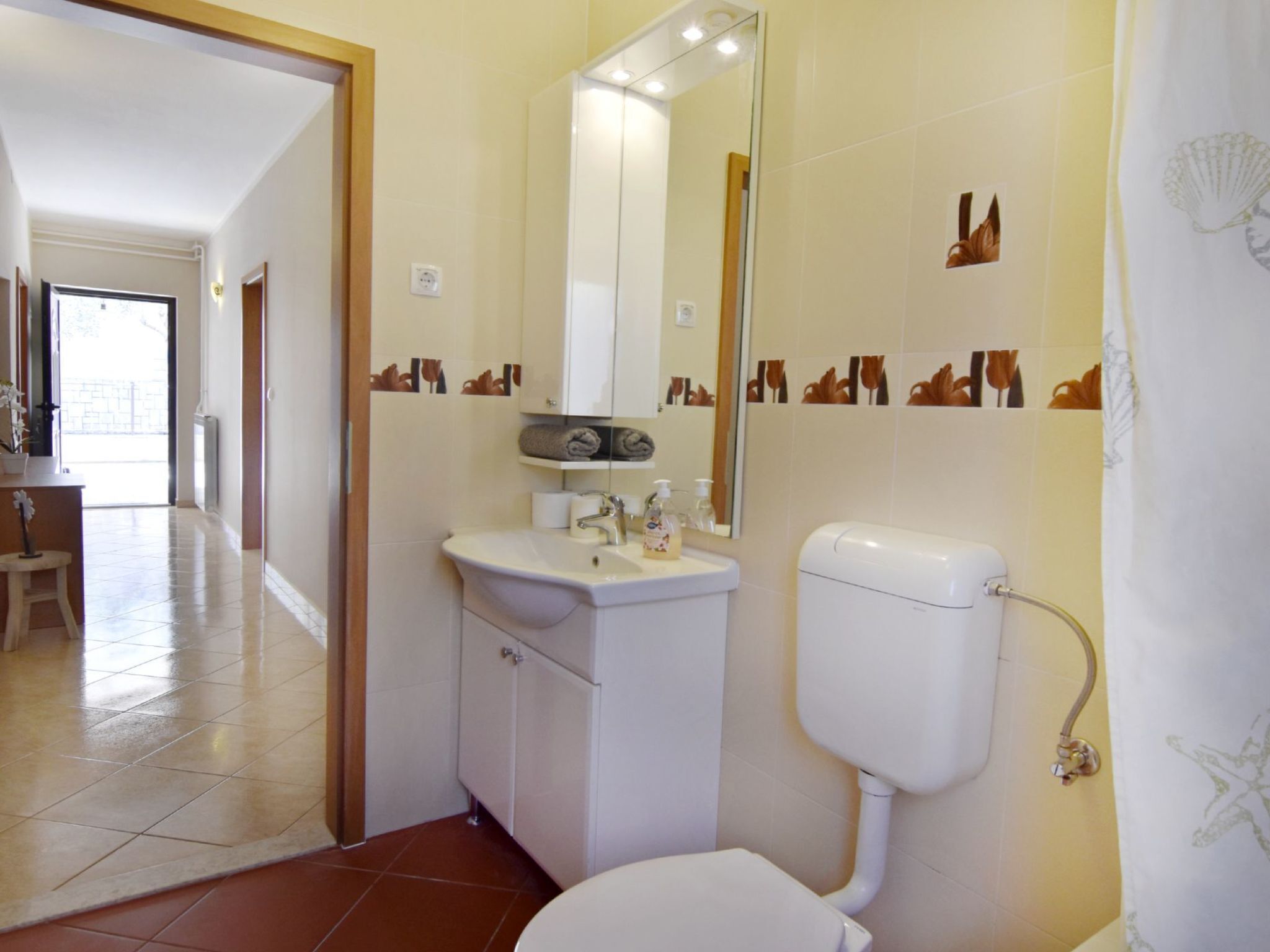 A bathroom with a toilet, sink, and mirror. There is a towel rack above the sink and a shower curtain with a floral pattern.