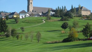 Um campo de golfe com uma torre de igreja, rodeado por edifícios residenciais.