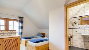 Quarto pequeno e aconchegante com cama no mezanino, escrivaninha de madeira e banheiro com parede azulejada e pia.