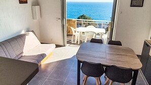 Ett rum med en soffa, ett matbord med stolar, utsikt över havet och en balkong med stolar.