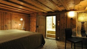 Een houten kamer met een bed, een stoel en een deur naar een badkamer.