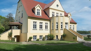 A large, two-story house with a red-tiled roof, multiple windows, and a small staircase leading to the entrance. - Wohnung im zweiten Obergeschoss des Gutshauses by Interhome (Gingst)