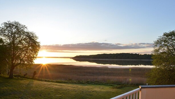 A deck with a railing overlooking a lake at sunrise. - Wohnung im zweiten Obergeschoss des Gutshauses by Interhome (Gingst)