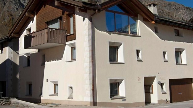 A two-story building with a balcony on the upper floor, a garage door on the right, and a clear view of the surrounding mountains. - Chesa La Capriola by Interhome (Sils Maria)