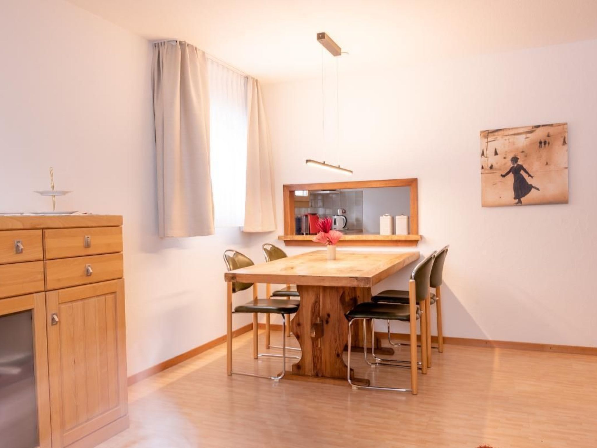Een eetruimte met een houten tafel, vier stoelen, een houten kast, een spiegel en een schilderij aan de muur.