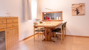 A dining area with a wooden table and four chairs, a wooden cabinet, a mirror, and a painting on the wall. - Chesa La Capriola by Interhome (Sils Maria)