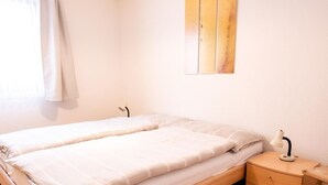 A double bed with a wooden frame, a bedside table with a lamp, and a small drawer unit. - Chesa La Capriola by Interhome (Sils Maria)