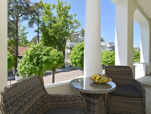 En balkong med flätade stolar och ett bord, en skål med frukt och utsikt över byggnader och träd.