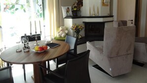Un comedor con una mesa redonda, sillas, un florero con flores y un osito de peluche sobre un cojín.