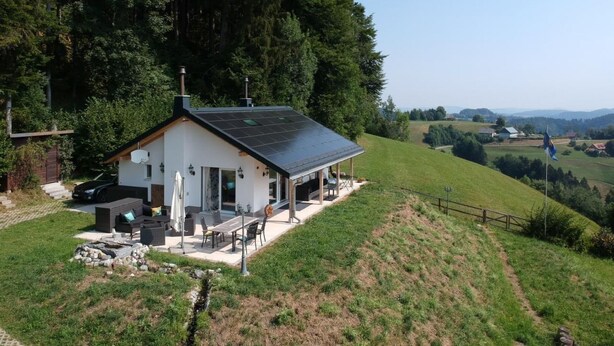 Una casa blanca con techo negro, paneles solares y un patio con mobiliario exterior.