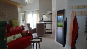 Una sala moderna con un sofá rojo, una mesita redonda y vistas a una cocina y montañas a través de un ventanal.