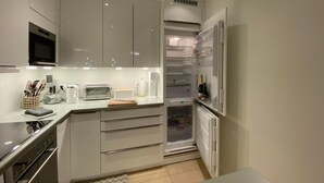 Una cocina moderna con armarios blancos, microondas integrado, tostadora y refrigerador.