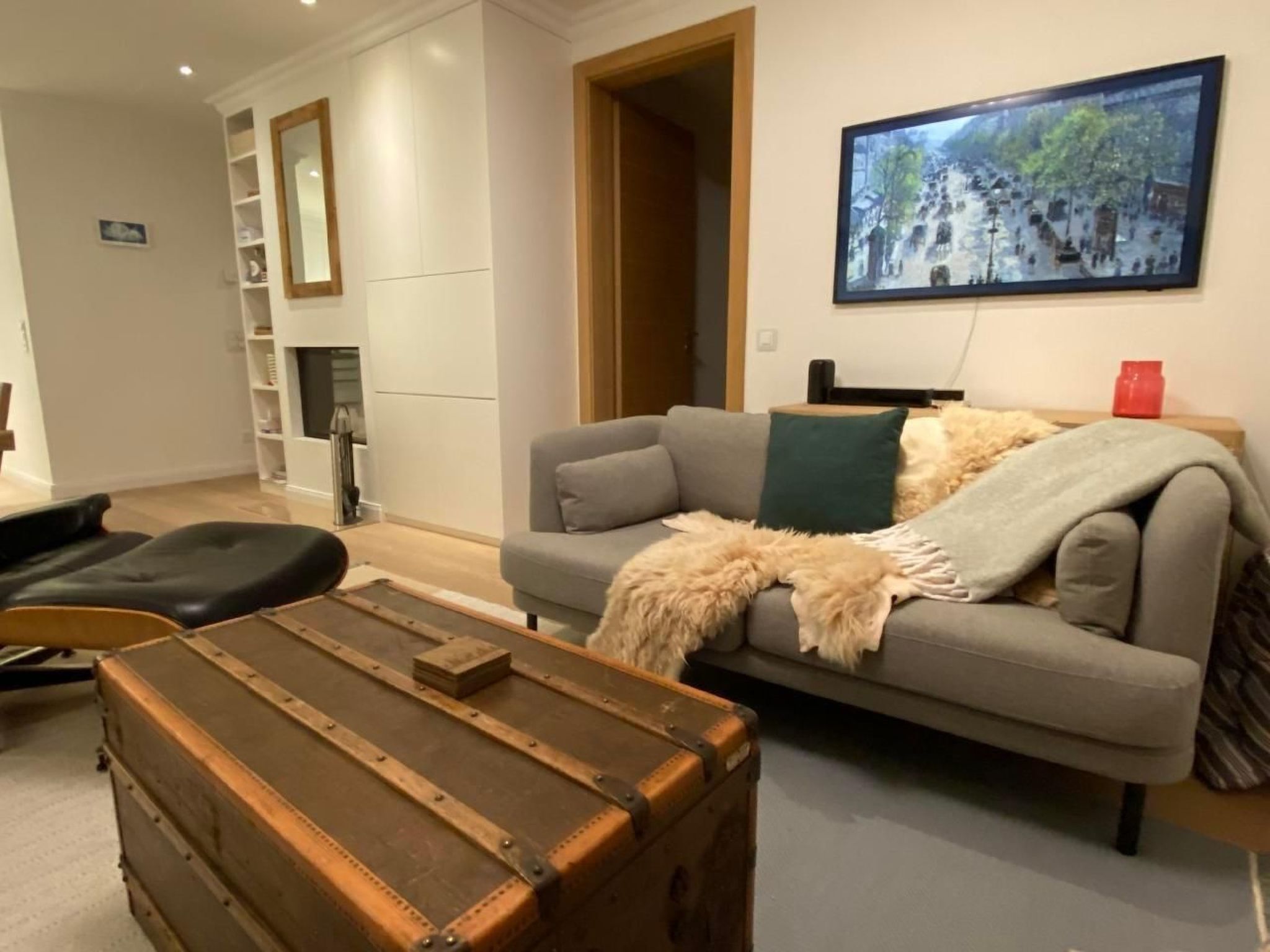 Una sala moderna con un sofá gris, un cofre de madera y un cuadro en la pared.