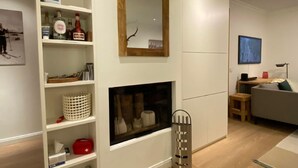 Una sala de estar moderna con chimenea, estanterías con diversos objetos, un espejo y un televisor.