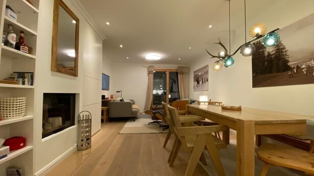 Un comedor con una mesa y sillas de madera, una araña y vistas a otra habitación.