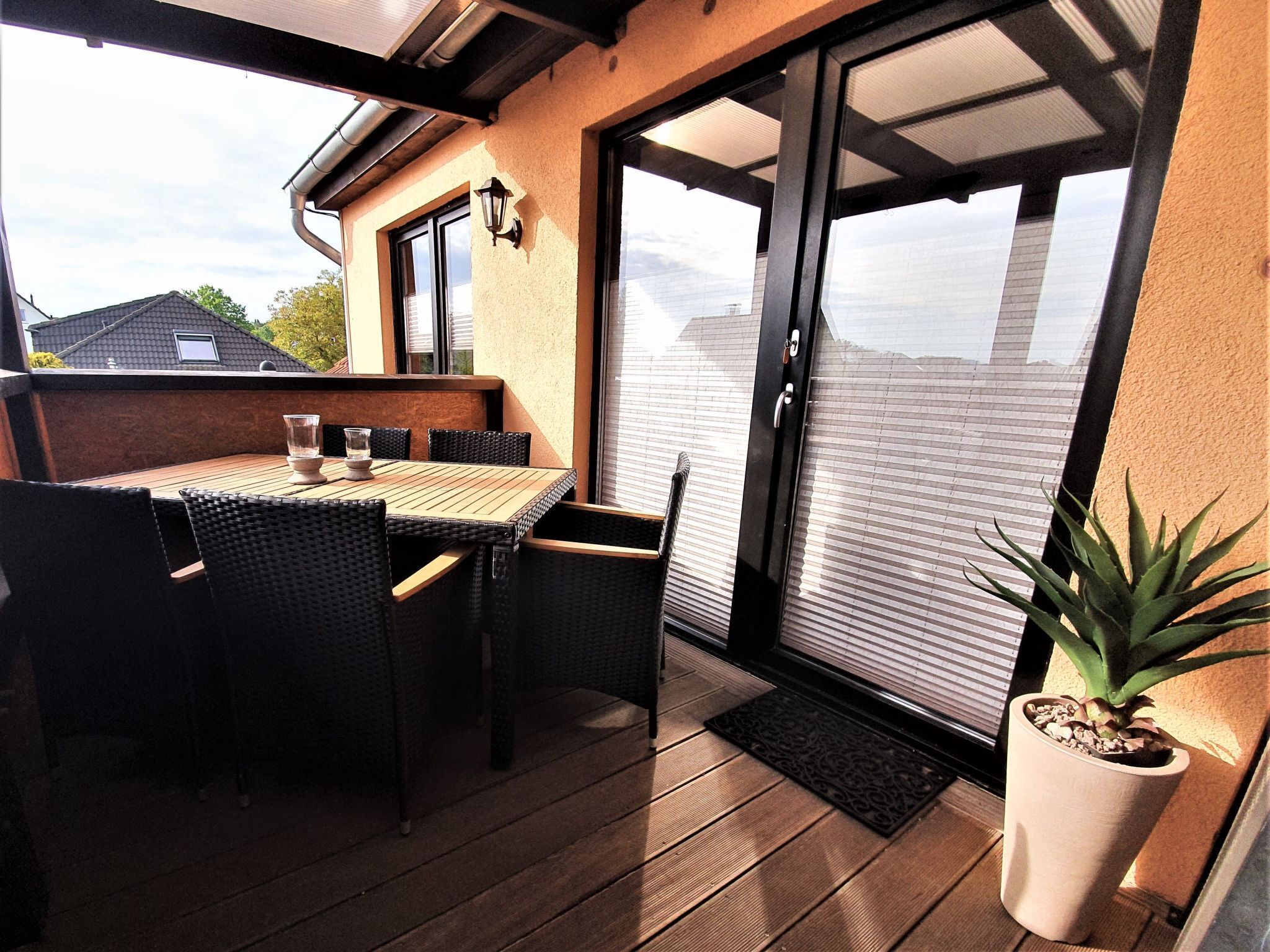 An outdoor patio with a table and chairs, a potted plant, and a sliding glass door leading to a balcony.