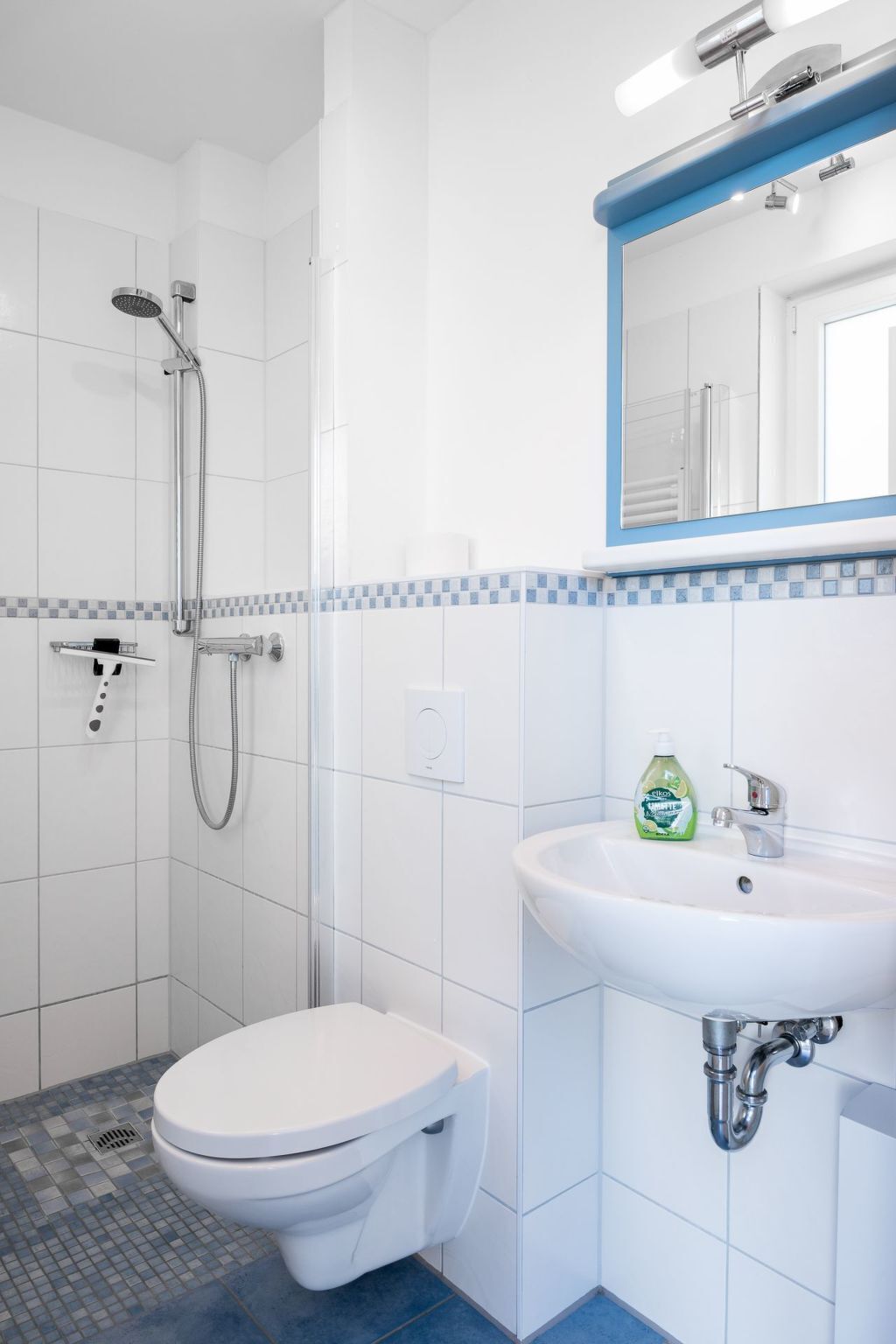 Un baño con inodoro blanco, lavamanos con espejo y zona de ducha.