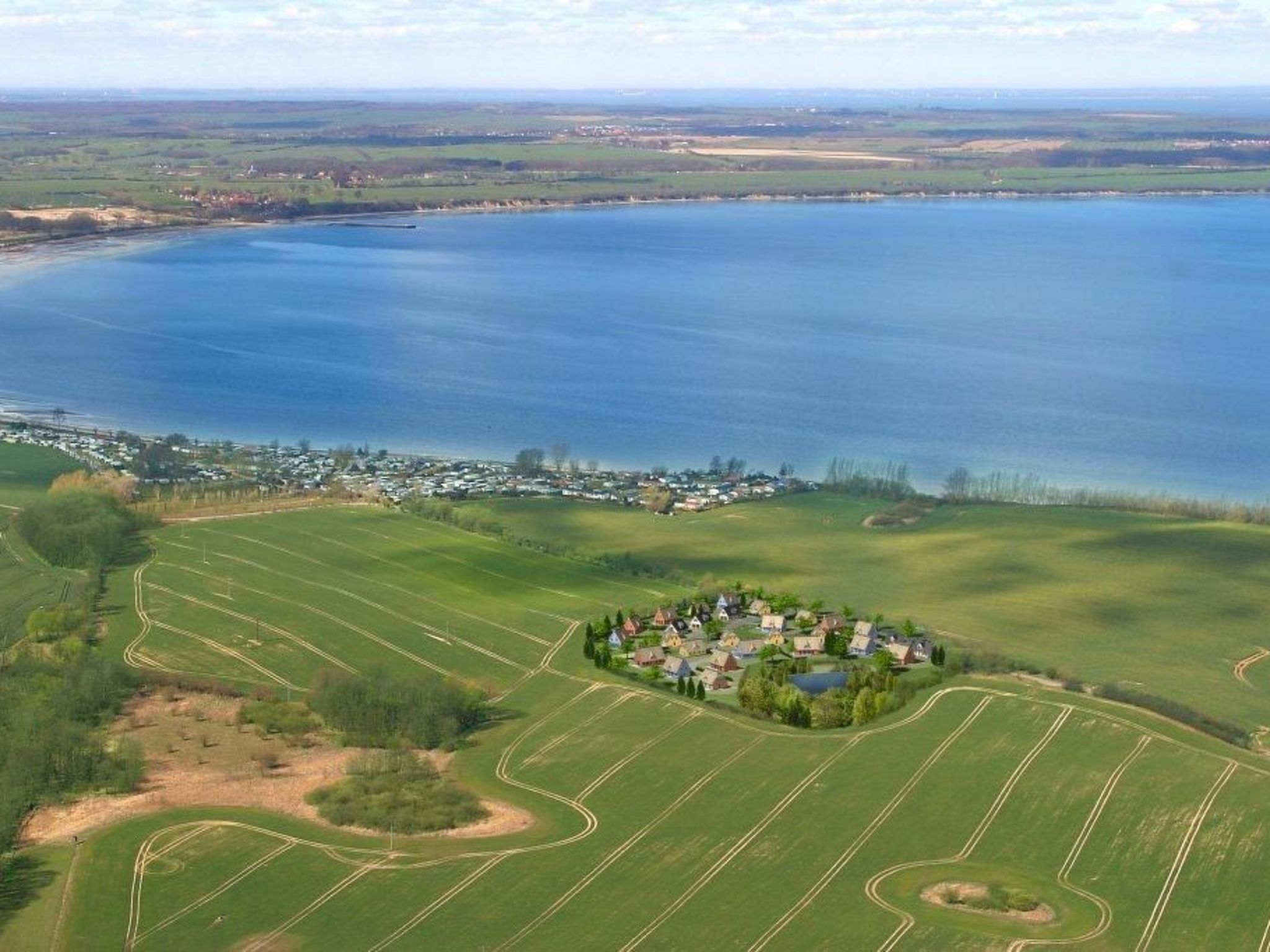Een luchtbeeld van een kustdorpje met een kleine groep huizen nabij een groot wateroppervlak.