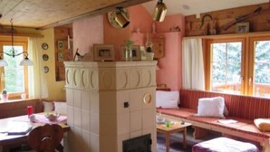 Ett mysigt rum med ett träpanelat tak, en inbyggd öppen spis, ett matbord med stolar, en bänk med kuddar och ett fönster med gardiner.