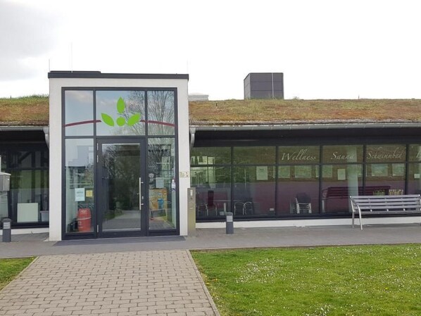 A modern building with a glass entrance, a green logo, and a sign reading "Wellness Sauna Schambiel".