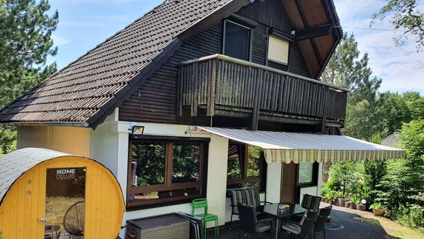 Una casa de madera de dos pisos con un porche cubierto, una sauna y mobiliario para exteriores.