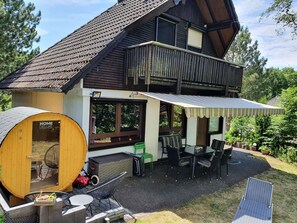 A two-story wooden house with a covered patio, a sauna, and outdoor seating.