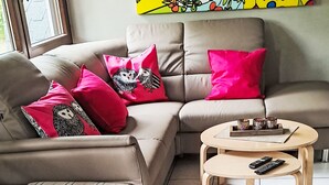 Una sala de estar moderna con sofá, reposapiés y mesa de centro, que incluye un control remoto y elementos decorativos.