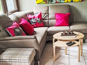 A modern living room with a sofa, ottoman, and coffee table, featuring a remote control and decorative items.