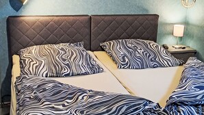 Cama doble con cabecera acolchada, dos almohadas estampadas con rayas de cebra, una lámpara de noche y un gancho fijado a la pared.