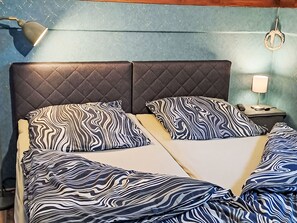 A double bed with a quilted headboard, two pillows with a zebra stripe pattern, a bedside lamp, and a wall-mounted hook.
