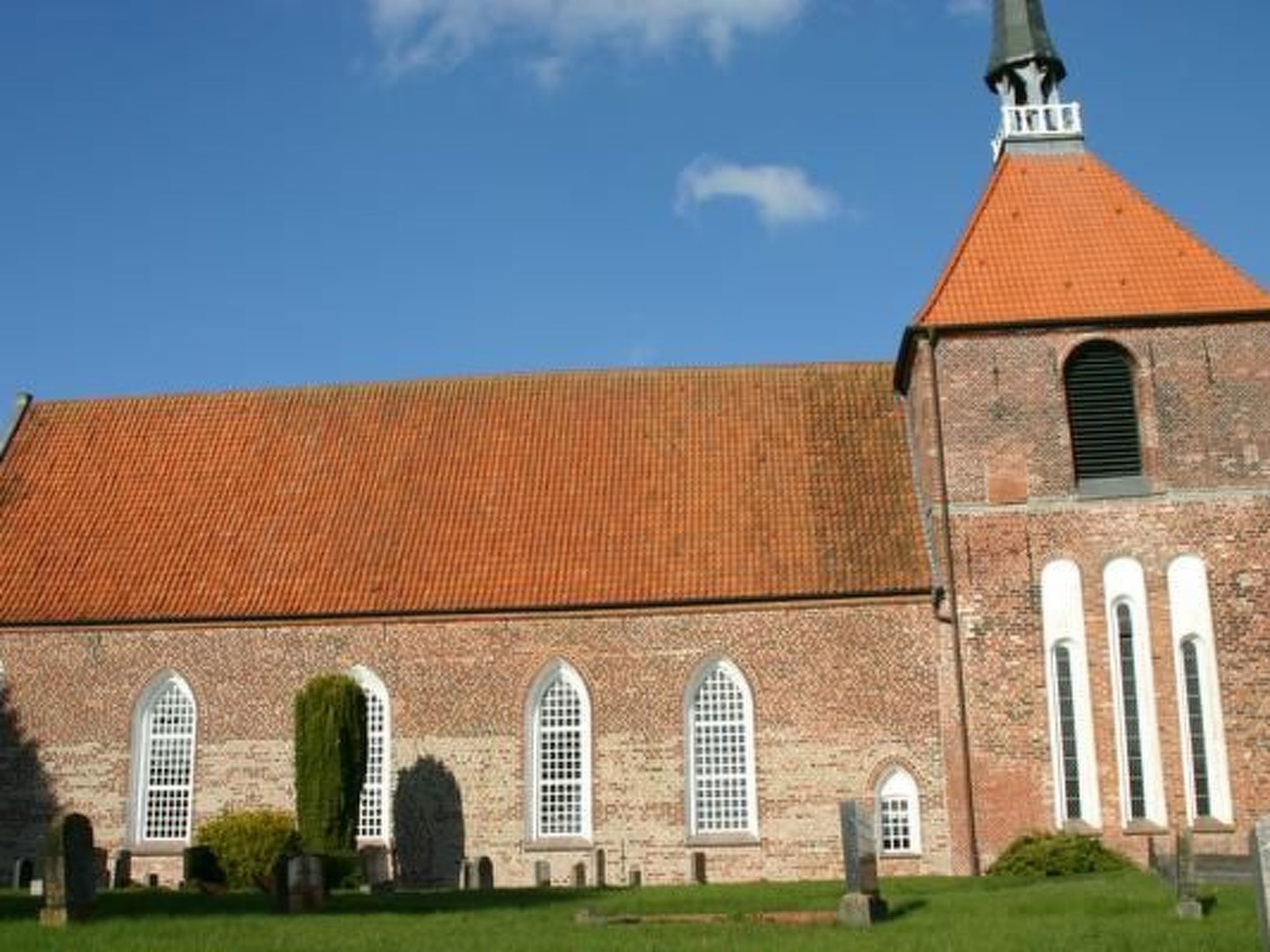 Een kerk met een gevel van baksteen, een pannendak en een hoge toren.