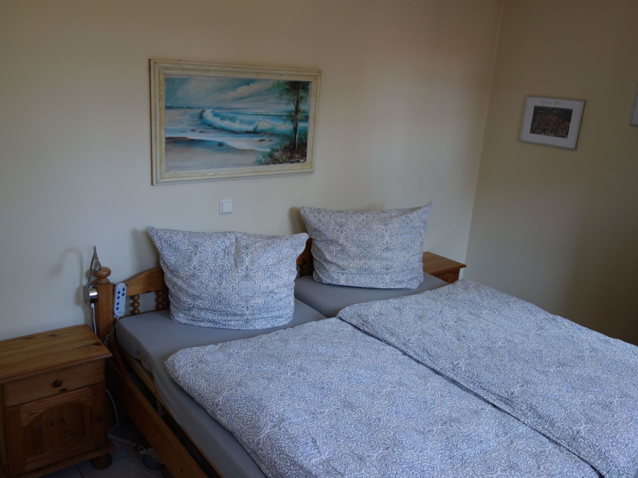 Une chambre à coucher avec un lit, deux oreillers, une table de chevet, une commode en bois et un tableau au mur.