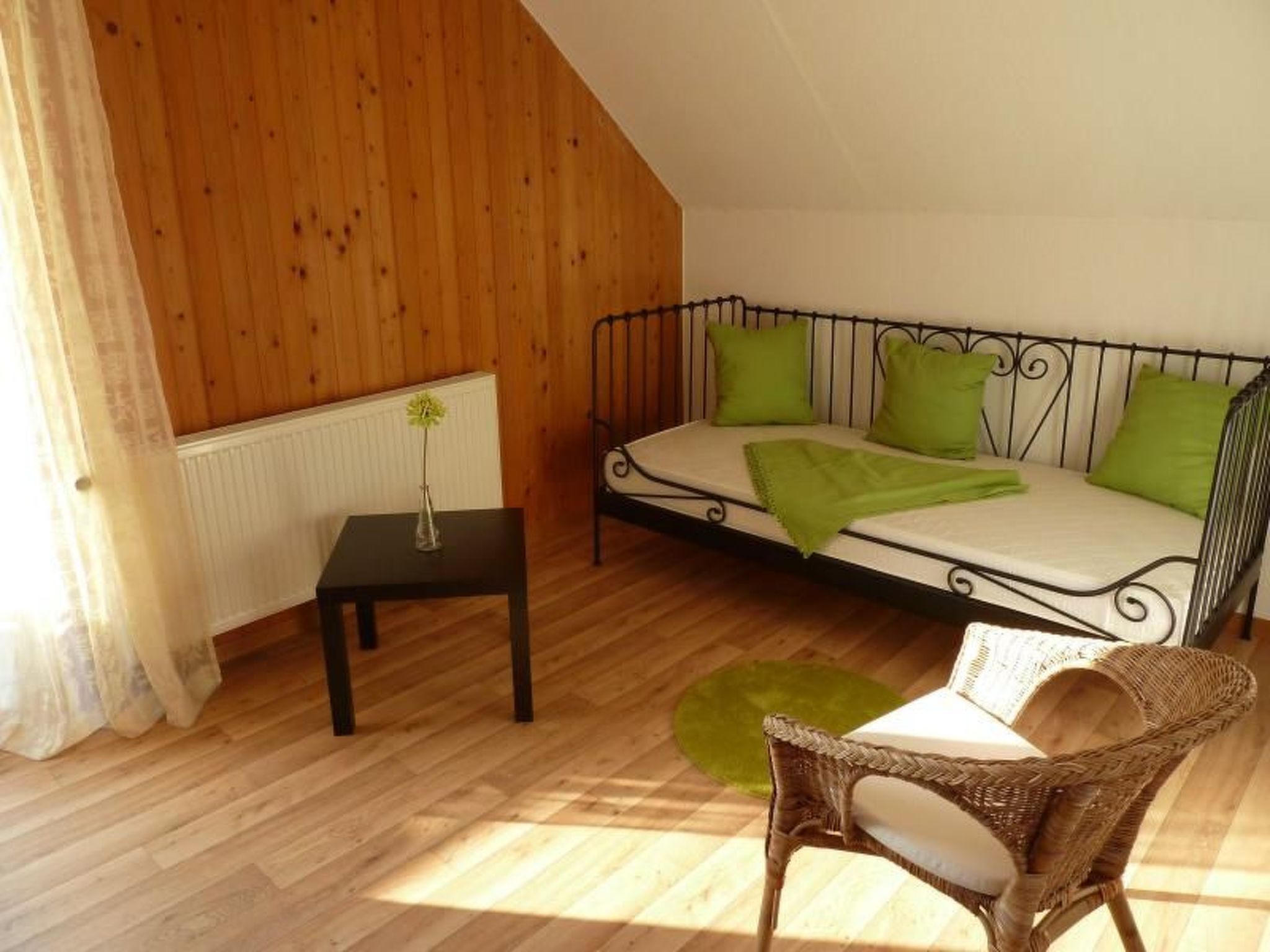 Ein gemütliches Zimmer mit einem Bett, einem kleinen Tisch mit einer Vase, einem Korbstuhl und Holzwänden.