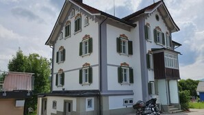 A multi-story building with a symmetrical facade, multiple windows with shutters, and a motorcycle parked in front. - Rhänstrasse 9 in Gais AR by Interhome (Gais)