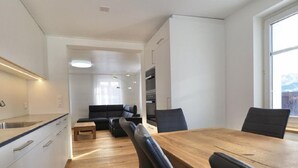 A modern kitchen with a wooden dining table and chairs, a built-in oven, and a seating area with a sofa and a coffee table. - Rhänstrasse 9 in Gais AR by Interhome (Gais)
