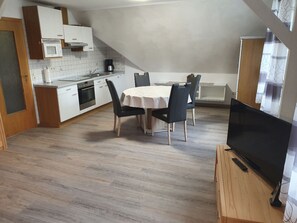 A compact kitchen with white cabinets, a microwave, and a coffee maker. There is a dining table with four chairs and a flat-screen TV on a wooden stand. - Komfortable Ferienwohnung in Werdum by Interhome (Bensersiel)