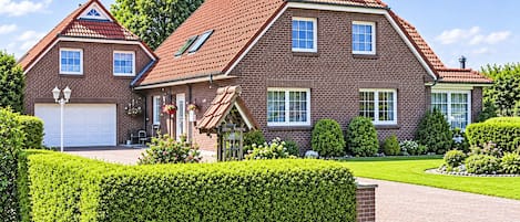 A two-story brick house with a red-tiled roof, a garage, and a well-maintained garden with hedges and a lawn.