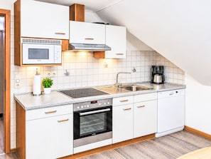 A modern kitchen with white cabinetry, a built-in microwave, a stove, and a coffee maker. - Komfortable Ferienwohnung in Werdum by Interhome (Bensersiel)