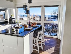 A modern kitchen with a central island, large windows, and a view of the city. - Strandvilla am Meer by Interhome (Großenbrode)