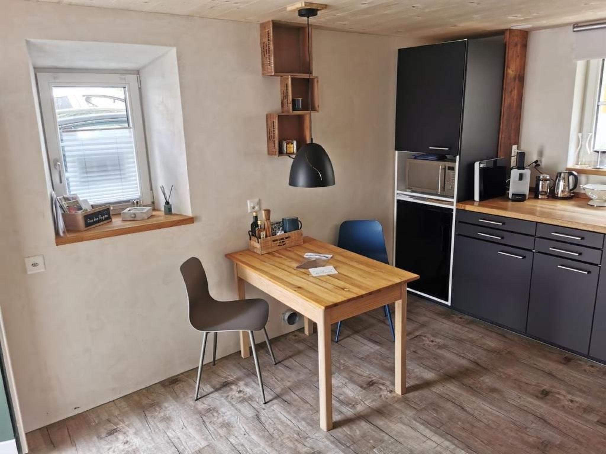 Eine kleine Küche mit Holztisch, zwei Stühlen, einer schwarzen Pendelleuchte und eingebauten Schränken.