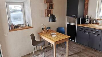 Eine kleine Küche mit Holztisch, zwei Stühlen, einer schwarzen Pendelleuchte und eingebauten Schränken.