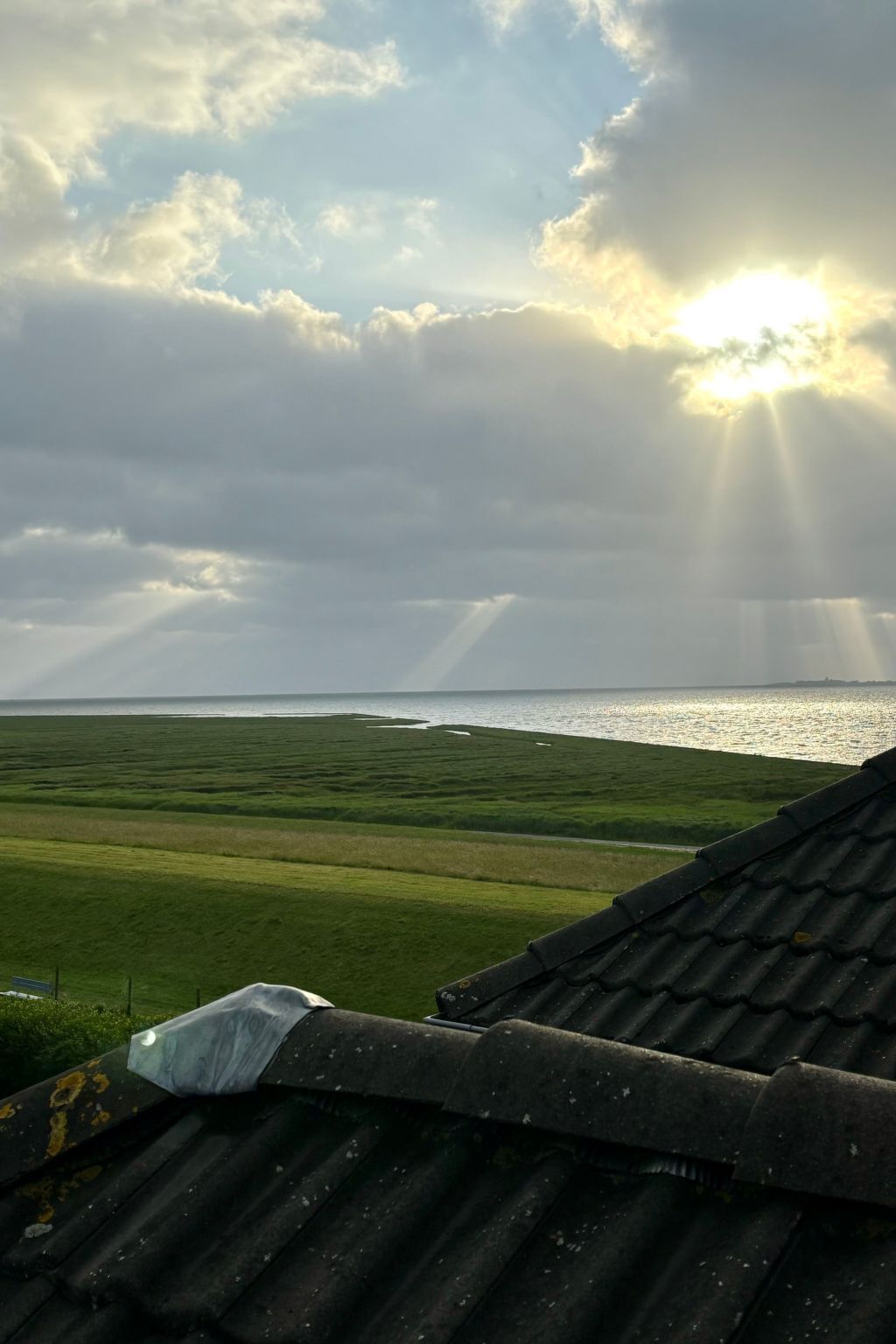 A view of a coastal landscape with a cloudy sky and sunlight breaking through.