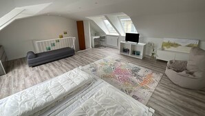 Amplio dormitorio tipo loft con una cama grande, un sofá, un televisor sobre un soporte blanco y una zona de escritorio.