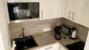 Una kitchenette compacta con microondas, tostadora, cafetera y lavabo.