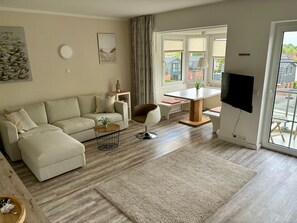 A modern living room with a sofa, a round coffee table, a TV, and a dining area with a table and chairs. - Nordseedüne II by Interhome (Cuxhaven)