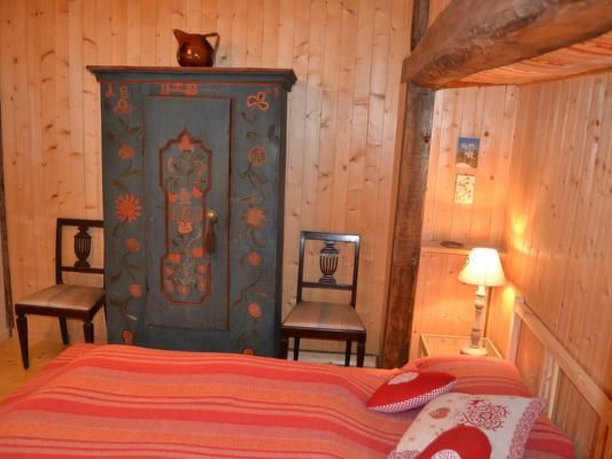 Ein gemütliches Zimmer mit einem Bett, zwei Stühlen, einer blumengemusterten Kommode und einer Lampe.