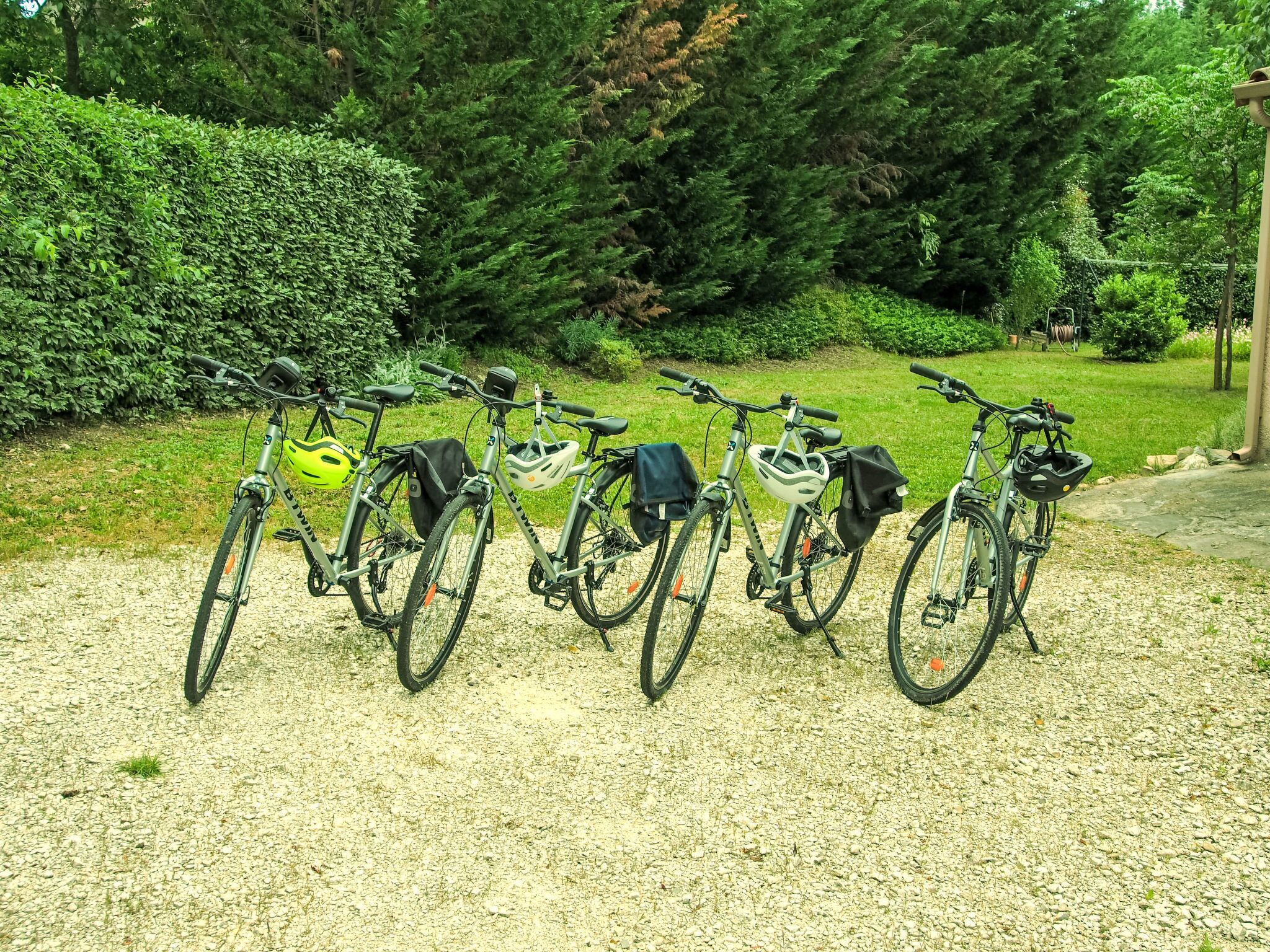 Vier fietsen geparkeerd op een grindpad, met een grasveld en dichte bomen op de achtergrond.