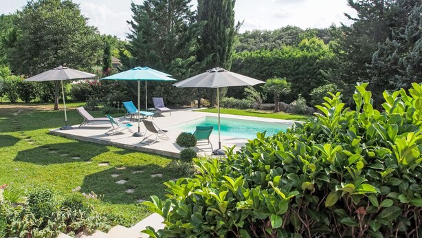 Un giardino con piscina, sedie a sdraio e ombrelloni.